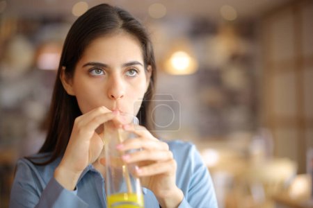 Photo for Front view of a distracted woman sipping orange juice with straw in a restaurant - Royalty Free Image