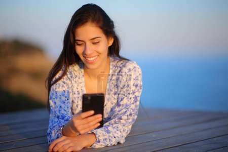 Téléchargez les photos : Portrait d'une femme heureuse utilisant un téléphone intelligent sur la côte - en image libre de droit