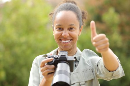 Téléchargez les photos : Vue de face portrait d'un photographe noir heureux avec les pouces levés - en image libre de droit