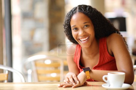 Téléchargez les photos : Heureuse femme noire riant en regardant la caméra dans un bar terrasse - en image libre de droit