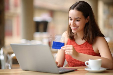 Téléchargez les photos : Femme heureuse avec ordinateur portable et carte de crédit achetant en ligne dans un bar terrasse - en image libre de droit