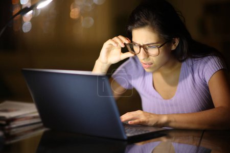 Téléchargez les photos : Femme utilisant des lunettes forçant la vue avec un ordinateur portable dans la nuit à la maison - en image libre de droit