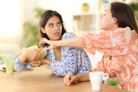 Foto de Mujer tratando de comer patatas fritas y amigo egoísta evitando en casa - Imagen libre de derechos