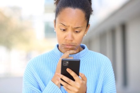 Photo for Front view portrait of a worried black woman checking phone in the street - Royalty Free Image