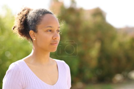 Foto de Retrato de una mujer negra seria en un parque mirando hacia otro lado - Imagen libre de derechos