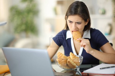 Téléchargez les photos : Glutton étudiant anxieux manger et étudier en ligne à la maison - en image libre de droit