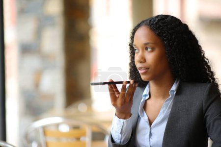 Negro mujer de negocios dictando mensaje por teléfono en una terraza cafetería