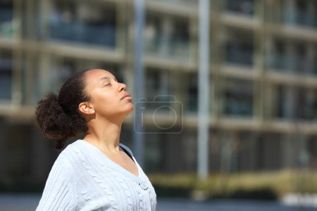 Téléchargez les photos : Femme noire sérieuse respirant l'air frais dans la rue - en image libre de droit