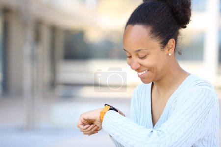 Photo for Black woman checking smartwatch smiling in the street - Royalty Free Image