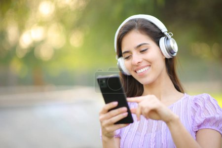Foto de Mujer feliz escuchando música usando auriculares y teléfonos inteligentes en un parque - Imagen libre de derechos