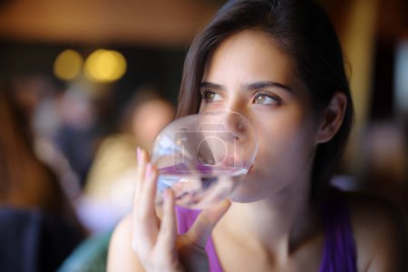 Photo for Distracted woman drinking water in a restaurant - Royalty Free Image