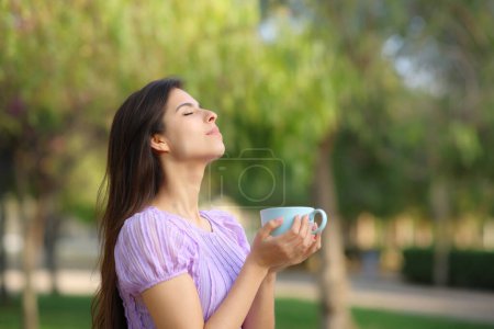 Téléchargez les photos : Profil d'une femme respirant du café dans un parc vert - en image libre de droit