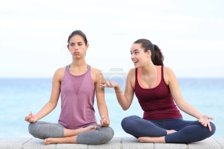 Téléchargez les photos : Vue de face portrait de yogi agacé essayant de faire du yoga avec un ami dérangeant sur la plage - en image libre de droit