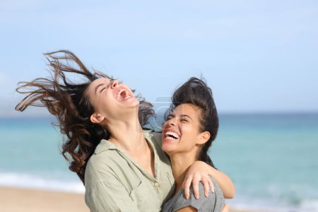 Foto de Dos divertidos mejores amigos riéndose hilarantemente abrazándose en la playa - Imagen libre de derechos