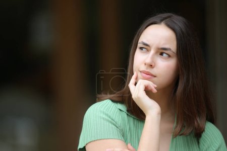 Photo for Doubtful woman wondering what to do looking at side outdoors - Royalty Free Image