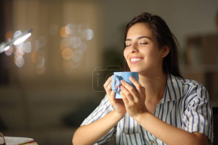 Foto de Mujer feliz bebiendo té y respirando en la noche en casa - Imagen libre de derechos
