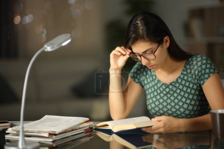 Téléchargez les photos : Femme avec des lunettes lisant un livre dans la nuit à la maison - en image libre de droit