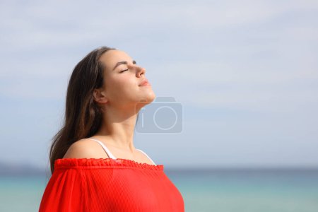 Téléchargez les photos : Femme détendue en rouge respirant de l'air frais sur la plage une journée d'été ensoleillée - en image libre de droit