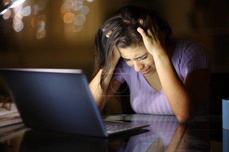 Téléchargez les photos : Triste femme se plaignant seul cheking ordinateur portable dans la nuit à la maison - en image libre de droit