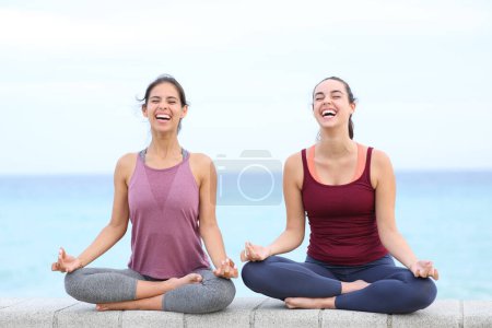 Téléchargez les photos : Deux yogis heureux riant faire du yoga sur la plage - en image libre de droit