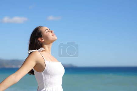 Téléchargez les photos : Femme en robe blanche respirant l'air frais seule sur la plage - en image libre de droit