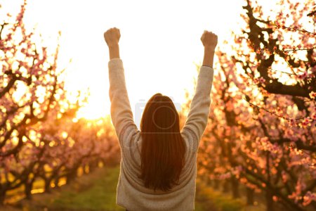 Foto de Retrato de una mujer feliz levantando brazos celebrando la salida del sol en un campo - Imagen libre de derechos