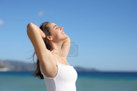 Téléchargez les photos : Profil d'une femme heureuse en dres blanches respirant de l'air frais avec aisselle cirée sur la plage - en image libre de droit