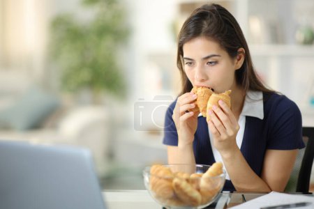 Foto de Mujer ansiosa desalentada comiendo panadería tratando de aliviar la ansiedad en casa - Imagen libre de derechos