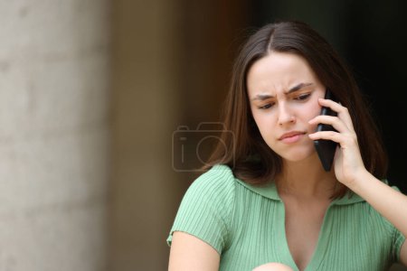 Photo for Confused woman talking on phone outdoors in the street - Royalty Free Image