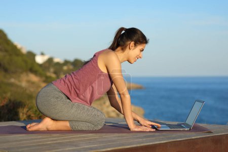 Téléchargez les photos : Yogi heureux préparant cours de yoga en ligne sur ordinateur portable sur la plage - en image libre de droit