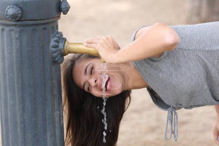 Foto de Mujer feliz riendo bebiendo agua de una fuente pública en un parque - Imagen libre de derechos