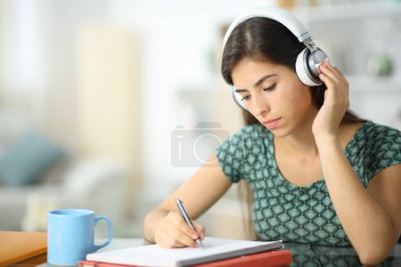 Téléchargez les photos : Étudiant portant un casque écoutant audioguide étudiant à la maison - en image libre de droit