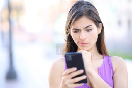 Photo for Front view of a suspicious woman checking phone in the street - Royalty Free Image