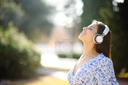 Téléchargez les photos : Portrait d'une femme heureuse écoutant un livre audio méditant avec un casque dans un parc - en image libre de droit