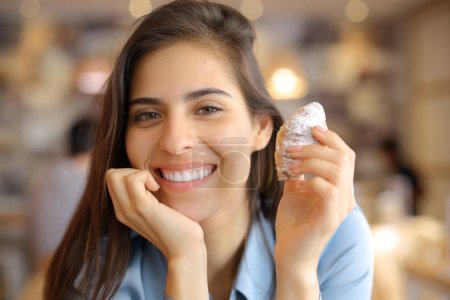Foto de Mujer feliz sonriendo sosteniendo bocadillo y mirando a la cámara en el interior de un bar - Imagen libre de derechos