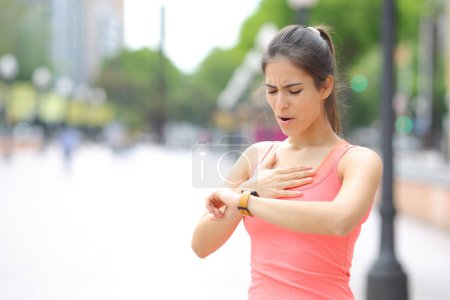 Photo for Tired runner checking time on smartwatch after running in the street - Royalty Free Image