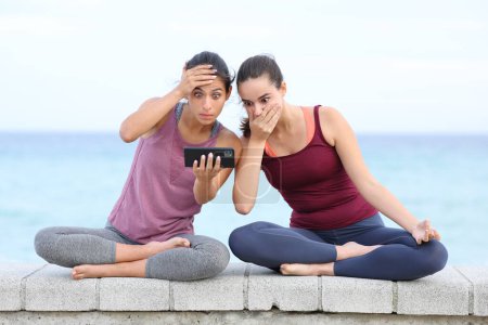 Téléchargez les photos : Vue de face portrait de deux yogis inquiets regardant difficile cours de yoga en ligne sur la plage - en image libre de droit