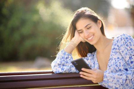 Téléchargez les photos : Femme heureuse vérifier le contenu du téléphone assis dans un jardin - en image libre de droit