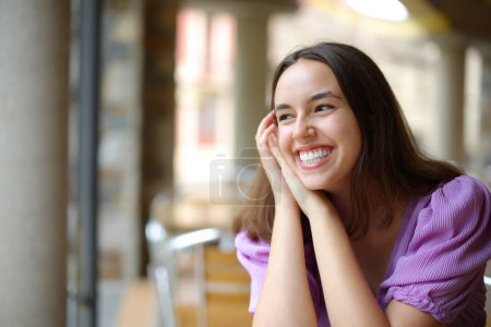 Téléchargez les photos : Femme heureuse riant seule dans un bar regardant côté - en image libre de droit
