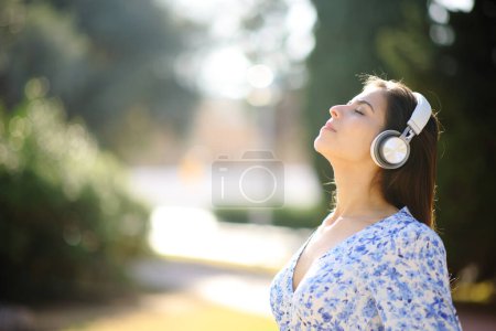 Téléchargez les photos : Profil d'une femme respirant de l'air frais et méditant écoutant un guide audio sur un casque dans un jardin - en image libre de droit
