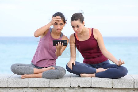 Foto de Yoguis sorprendidos viendo yoga tutorial difícil en el teléfono inteligente en la playa - Imagen libre de derechos