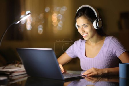 Foto de Mujer feliz con auriculares viendo la película en el ordenador portátil en la noche en casa - Imagen libre de derechos