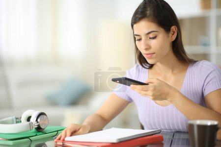 Téléchargez les photos : Étudiant utilisant le téléphone pour prendre une photo de notes apprenant à la maison - en image libre de droit