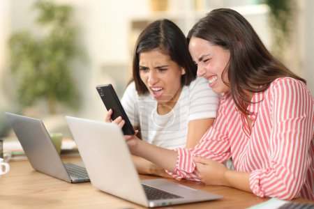 Two disgusted women checking nasty content on phone at home