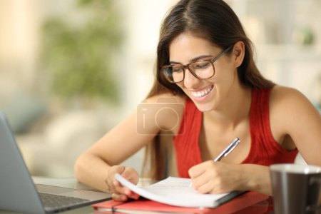 Foto de Estudiante feliz con anteojos tomando notas estudiando en casa - Imagen libre de derechos