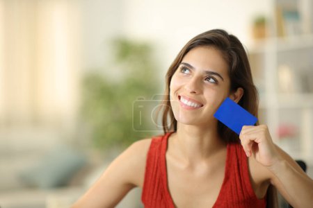 Téléchargez les photos : Femme heureuse rêvant et montrant la carte de crédit vierge à la maison - en image libre de droit