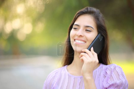 Téléchargez les photos : Femme heureuse marchant et parlant au téléphone dans un parc ou un jardin - en image libre de droit