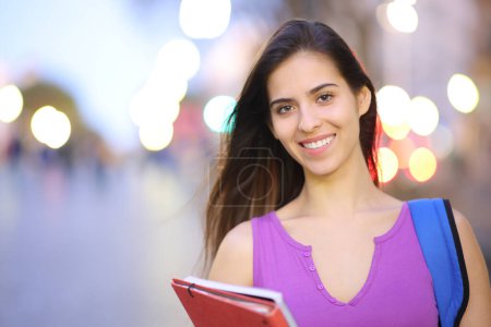 Porträt einer glücklichen Studentin, die abends auf der Straße posiert und in die Kamera blickt