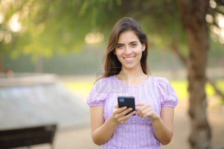 Photo for Front view portrait of a happy woman holding phone in a park - Royalty Free Image