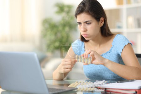Gestresste Studentin nimmt Pillen und lernt zu Hause mit Laptop online